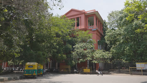 Außenansicht-Eines-Traditionellen-Rosafarbenen-Gebäudes-In-Bangalore,-Indien,-Davor-Geparktes-Autorikscha-Taxi