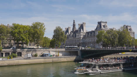 Touristenboot-Fährt-Unter-Der-Pont-D&#39;Arcole-Brücke-Hindurch-Und-überquert-Die-Seine-Mit-Dem-Hotel-De-Ville-In-Paris,-Frankreich,-Mit-Touristen-Und-Verkehr