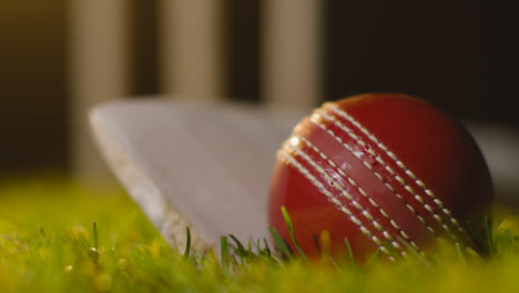 Cricket-Stillleben-Mit-Nahaufnahme-Von-Ball-Und-Schläger,-Die-Im-Gras-Vor-Stümpfen-Liegen-3