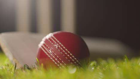 Cricket-Stillleben-Mit-Nahaufnahme-Von-Ball-Und-Schläger,-Die-Im-Gras-Vor-Stümpfen-Liegen