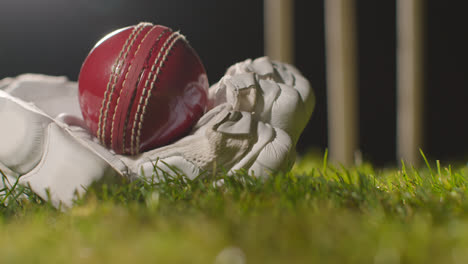 Cricket-Stillleben-Mit-Nahaufnahme-Eines-Balls,-Der-Im-Handschuh-Auf-Gras-Vor-Stümpfen-Liegt