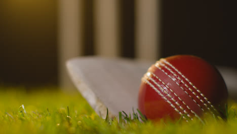 Cricket-Stillleben-Mit-Nahaufnahme-Von-Ball-Und-Schläger,-Die-Im-Gras-Vor-Stümpfen-Liegen-4