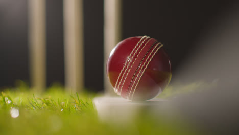 Cricket-Stillleben-Mit-Nahaufnahme-Eines-Balls-Auf-Einem-Schläger,-Der-Im-Gras-Vor-Stümpfen-Liegt-2