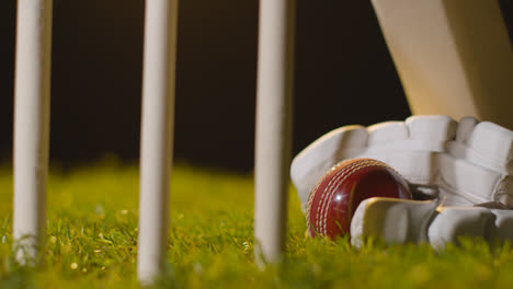 Cricket-Stillleben-Mit-Nahaufnahme-Eines-Schlägerballs-Und-Handschuhen,-Die-Im-Gras-Hinter-Stümpfen-Liegen