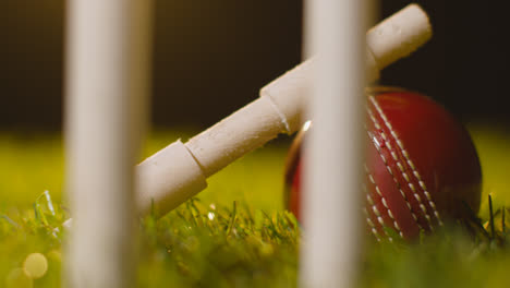 Cricket-Stillleben-Mit-Nahaufnahme-Von-Kautionen,-Die-Auf-Einem-Ball-Im-Gras-Hinter-Baumstümpfen-Ruhen
