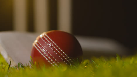 Cricket-Stillleben-Mit-Nahaufnahme-Von-Ball-Und-Schläger,-Die-Im-Gras-Vor-Stümpfen-Liegen-2