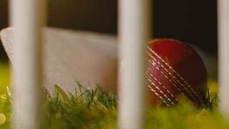 Cricket-Stillleben-Mit-Nahaufnahme-Von-Ball-Und-Schläger,-Die-Im-Gras-Hinter-Stümpfen-Liegen-5