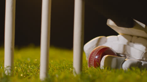 Cricket-Stillleben-Mit-Nahaufnahme-Eines-Schlägerballs-Und-Handschuhen,-Die-Im-Gras-Hinter-Stümpfen-Liegen-2