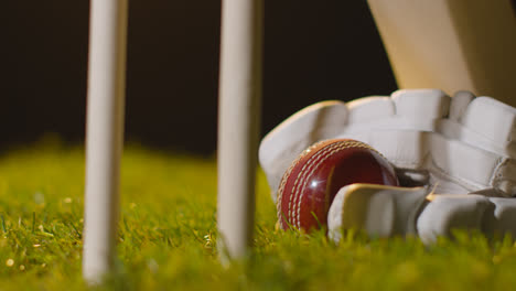 Cricket-Stillleben-Mit-Nahaufnahme-Eines-Schlägerballs-Und-Handschuhen,-Die-Im-Gras-Hinter-Stümpfen-Liegen-1