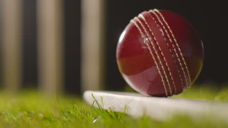 Cricket-Stillleben-Mit-Nahaufnahme-Eines-Balls-Auf-Einem-Schläger,-Der-Im-Gras-Vor-Stümpfen-Liegt-1