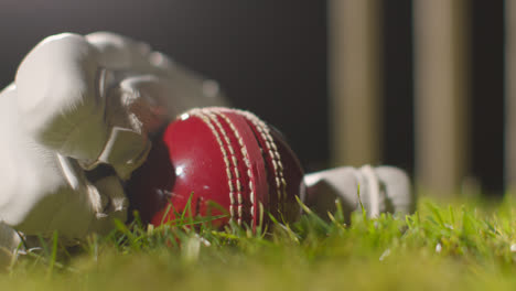Cricket-Stillleben-Mit-Nahaufnahme-Eines-Balls,-Der-Im-Handschuh-Auf-Gras-Vor-Stümpfen-Liegt-3