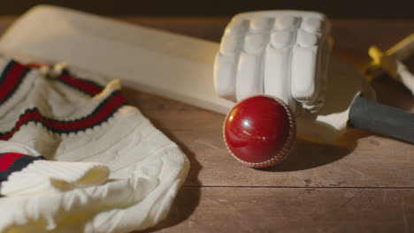Cricket-Stillleben-Mit-Nahaufnahme-Von-Schlägerhandschuhen,-Stümpfen,-Pullover-Und-Kautionen,-Während-Der-Ball-In-Den-Rahmen-Rollt
