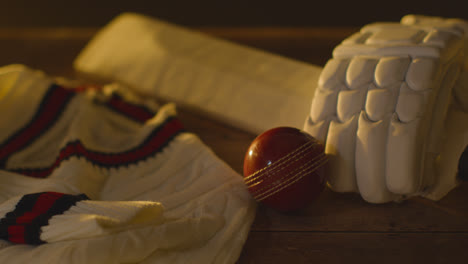Cricket-Still-Life-With-Close-Up-Of-Bat-Ball-Gloves-Stumps-Jumper-And-Bails-Lying-On-Wooden-Surface-In-Locker-Room-2