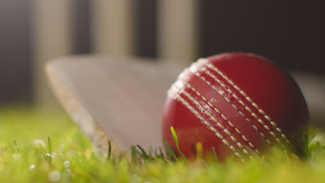 Cricket-Stillleben-Mit-Nahaufnahme-Von-Ball-Und-Schläger,-Die-Im-Gras-Vor-Stümpfen-Liegen-1
