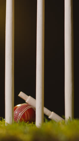 Vertical-Video-Cricket-Still-Life-With-Close-Up-Of-Bails-Resting-On-Ball-In-Grass-Behind-Stumps-2