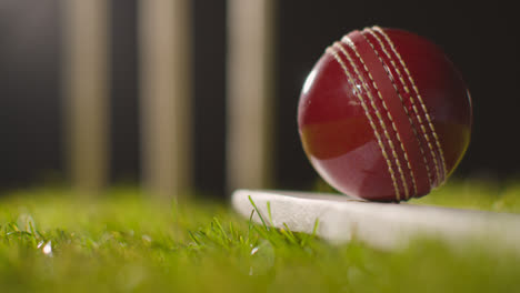 Cricket-Stillleben-Mit-Nahaufnahme-Eines-Balls-Auf-Einem-Schläger,-Der-Im-Gras-Vor-Stümpfen-Liegt