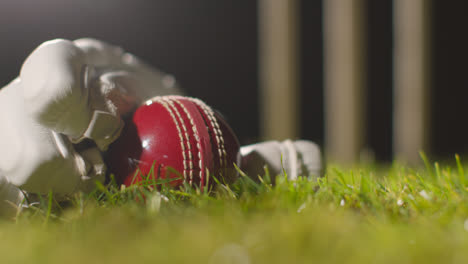 Cricket-Stillleben-Mit-Nahaufnahme-Eines-Balls,-Der-Im-Handschuh-Auf-Gras-Vor-Stümpfen-Liegt-2
