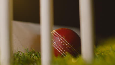 Cricket-Stillleben-Mit-Nahaufnahme-Von-Ball-Und-Schläger,-Die-Im-Gras-Hinter-Stümpfen-Liegen-1
