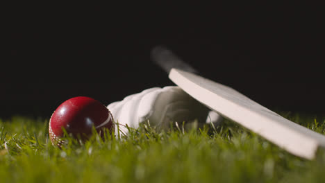 Studio-Cricket-Still-Life-With-Close-Up-Of-Ball-Rolling-Next-To-Bat-And-Glove-Lying-In-Grass-2