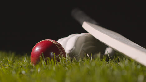 Studio-Cricket-Still-Life-With-Close-Up-Of-Ball-Rolling-Next-To-Bat-And-Glove-Lying-In-Grass