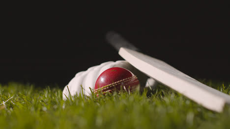 Studio-Cricket-Still-Life-With-Close-Up-Of-Ball-Rolling-Next-To-Bat-And-Glove-Lying-In-Grass-1