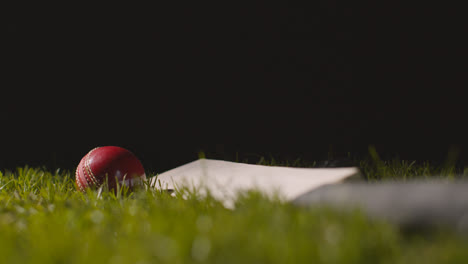 Studio-Cricket-Stillleben-Mit-Nahaufnahme-Eines-Balls,-Der-Auf-Einen-Im-Gras-Liegenden-Schläger-Rollt