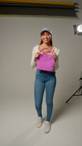Vertical-Video-Of-Female-Social-Media-Influencer-Producing-User-Generated-Content-In-Studio-Modelling-Purple-Bag