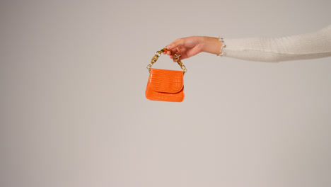 Close-Up-Of-Female-Social-Media-Influencer-Producing-User-Generated-Content-Holding-Out-Orange-Fashion-Handbag-2