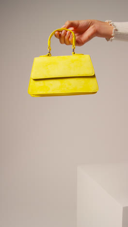 Close-Up-Vertical-Video-Of-Female-Social-Media-Influencer-Producing-User-Generated-Content-Holding-Out-Yellow-Fashion-Handbag