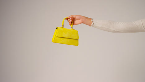 Close-Up-Of-Female-Social-Media-Influencer-Producing-User-Generated-Content-Holding-Out-Yellow-Fashion-handbag