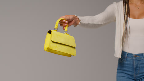Close-Up-Of-Female-Social-Media-Influencer-Producing-User-Generated-Content-Holding-Out-Yellow-Fashion-Handbag-1
