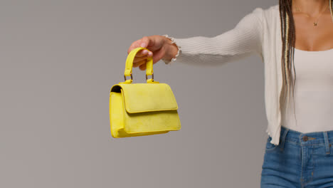 Close-Up-Of-Female-Social-Media-Influencer-Producing-User-Generated-Content-Holding-Out-Yellow-Fashion-Handbag