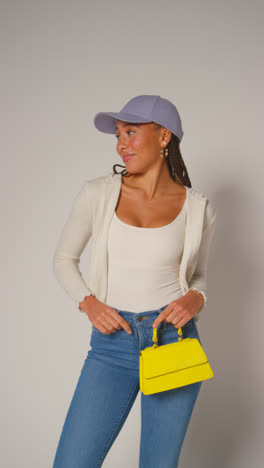 Vertical-Video-Of-Female-Social-Media-Influencer-Producing-User-Generated-Content-In-Studio-Modelling-Yellow-Handbag