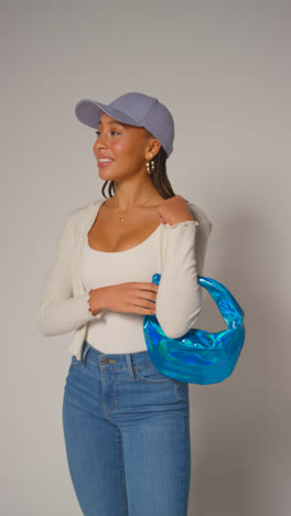 Vertical-Video-Of-Female-Social-Media-Influencer-Producing-User-Generated-Content-In-Studio-Catching-And-Modelling-Blue-Handbag