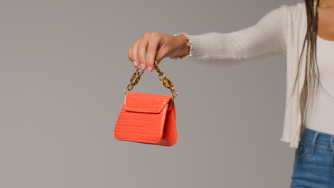 Close-Up-Of-Female-Social-Media-Influencer-Producing-User-Generated-Content-Holding-Out-Orange-Fashion-Handbag