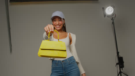 Female-Social-Media-Influencer-Producing-User-Generated-Content-In-Studio-Holding-Variety-Of-Different-Fashion-Handbags