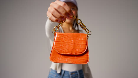 Weibliche-Social-Media-Influencerin-Produziert-Benutzergenerierte-Inhalte-Und-Modelliert-Eine-Orangefarbene-Modehandtasche-Im-Studio