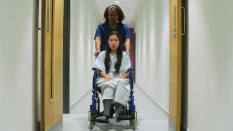 Enfermera-empuja-paciente-en-silla-de-ruedas-en-corredor