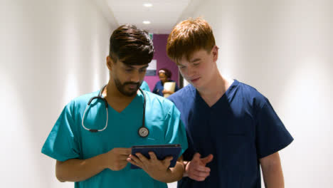 Two-Medical-Staff-Using-Tablet-Walking-In-Corridor