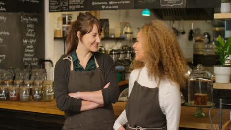 Dos-mujeres-felices-baristas-en-un-café-sonriendo-el-uno-al-otro