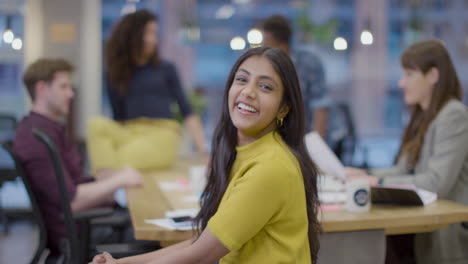 Portrait-of-Smiling-woman-in-office-with-colleagues-working-in-background-
