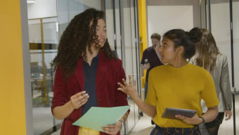 Dos-mujeres-colegas-de-negocios-hablando-en-un-corredor