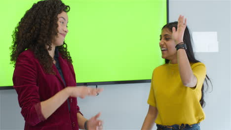 Two-Businesswomen-Presenting-To-Colleagues-With-Green-Screen-And-High-Fiving