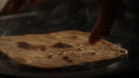 Slow-motion-close-up-of-steaming-hot-roti-cooked-on-a-cast-iron-pan-and-flipping-with-bare-hands