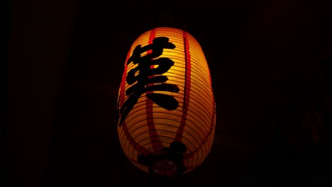 Closeup-of-an-illuminated-Chinese-lantern-lamp-with-the-letter-KA-written-in-Chinese-shaking-in-the-wind