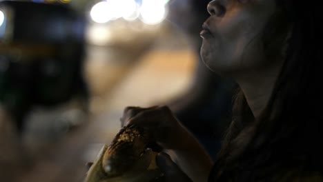 Close-up-of-an-Asian-south-Indian-woman-eating-corn-from-a-cob-during-evening-with-the-traffic-in-the-background-