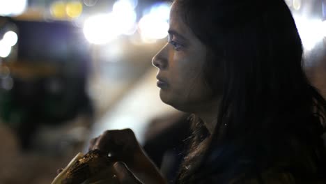 Close-up-of-an-Asian-south-Indian-woman-eating-corn-from-a-cob-during-evening-with-the-traffic-in-background-