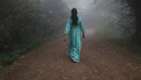 Wide-angle-shot-of-a-woman-wearing-a-dress-walking-through-thick-fog-in-a-forest-during-early-morning