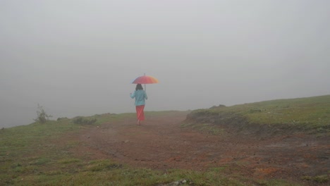 Wide-angle-shot-of-a-South-Indian-woman-walking-with-a-colorful-umbrella-on-a-hill-top-during-a-foggy-morning