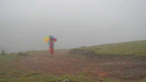Wide-angle-of-South-Indian-woman-walking-with-a-colorful-umbrella-on-a-hill-top-during-a-foggy-morning